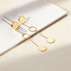 Minimalist gold geometric tassel earrings hanging on a notebook under soft window light