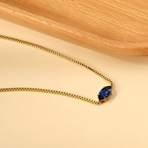 Dettaglio collana in oro con ciondolo a gemma blu taglio marquise su vassoio in legno