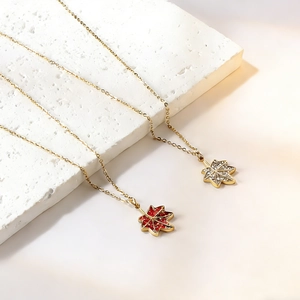Détail de colliers feuille d'érable en or avec cristaux rouges et blancs sur pierre