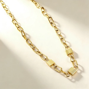 Macro detail of paperclip link chain with three textured square lock pendants in gold