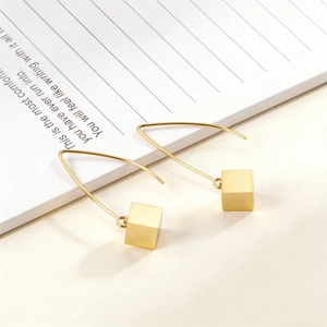 Detail of minimalist gold cube earrings with long triangular hooks on white paper