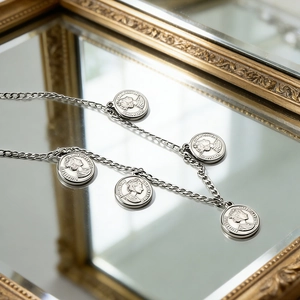 Detail of silver Cuban chain necklace with five vintage portrait coin charms on a mirror