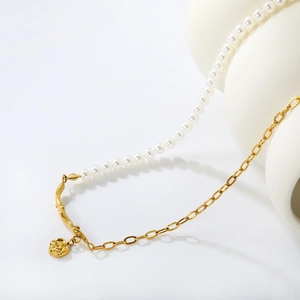 Elegant gold rose pendant necklace with white pearls and metal links on ceramic vase