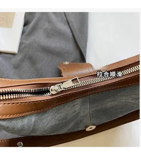 Détail de la fermeture éclair en métal argenté et bordure en cuir brun du sac en jean
