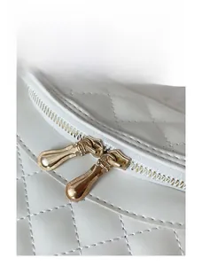 Detail shot of the gold dual zipper and quilted texture on white PU shoulder bag