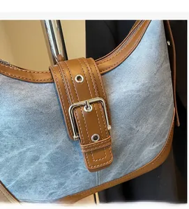 Détail du sac hobo en denim bleu avec lanières en cuir marron et boucles métalliques