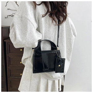 Sac bandoulière en cuir verni noir brillant avec mini pochette porté par un mannequin