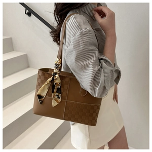 Detail of a brown tote bag featuring checkered textures and a baroque print silk scarf handle