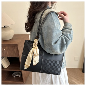 Chic black tote bag with checkered panel and silk scarf on shoulder of a model