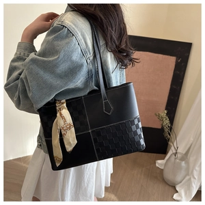 Detail of black patchwork tote bag with woven texture and decorative silk scarf charm