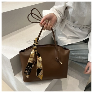 Close-up of caramel leather tote bag handle with elegant black and gold silk scarf detail
