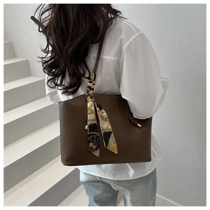 Borsa tote marrone con foulard in seta sul manico, indossata da modella su scale bianche