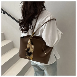 Detail of deep brown leather tote bag with elegant floral scarf wrapped on the handle