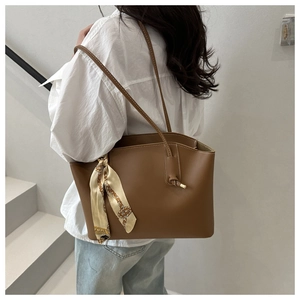 Detail of a brown leather tote bag with a decorative scarf on shoulder of a model