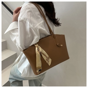 Detail of tan leather tote bag with silk scarf handle on model in minimalist setting