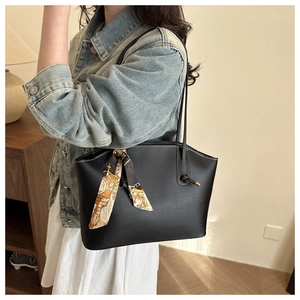 Dettaglio di borsa tote nera con manici a nodo e foulard decorativo in seta gialla