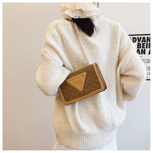 Detail einer braunen Lederumhängetasche mit M-Muster und Goldkette auf weißem Pullover