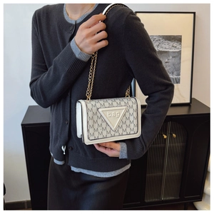 Detail der eleganten beigen Klapptasche mit grauen M-Mustern und goldener Kettenriemen
