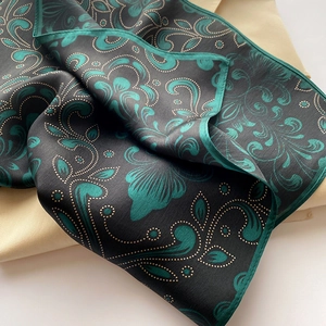 Detail of luxury silk scarf showing intricate green paisley pattern and hemmed edges
