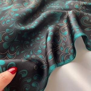 Close-up of luxury silk scarf showing emerald green floral pattern and hem details