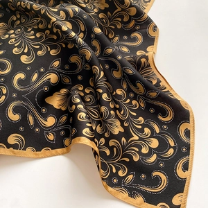 Close-up of elegant silk scarf with gold paisley pattern on smooth black fabric