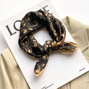 Detail of luxury silk scarf with black and gold paisley print on a beige blazer