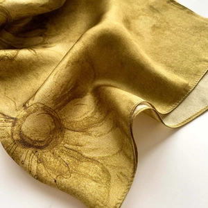 Gros plan d'un foulard en soie jaune moutarde à motif floral avec bords roulés et satinés