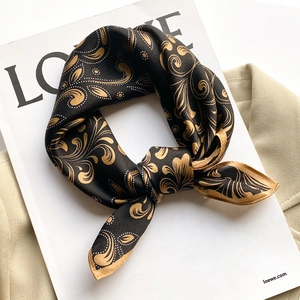 Elegant black and gold silk square scarf with paisley pattern on a beige coat