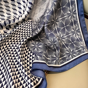 Detailed view of geometric pattern silk scarf with navy blue borders and satin finish
