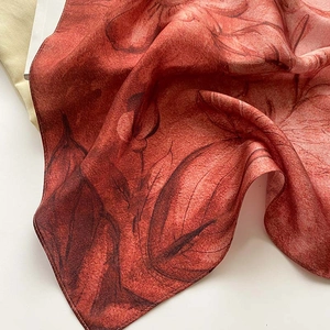Gros plan détaillé du foulard en soie marron rouge à fleurs montrant la texture du tissu