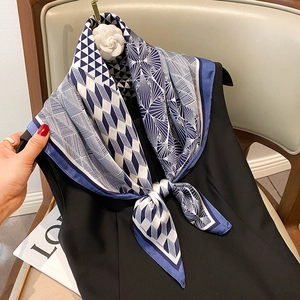 Close-up of elegant blue geometric faux silk scarf tied on a black dress with flower brooch