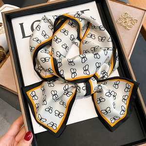 Dettaglio di un foulard in seta crema con motivi di farfalle nere annodato a fiocco
