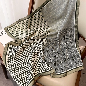 Detail of silk satin scarf with olive green geometric patterns draped on a chair