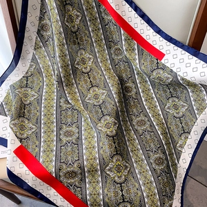 Detalle de bufanda cuadrada de seda con estampado paisley sobre una silla de madera