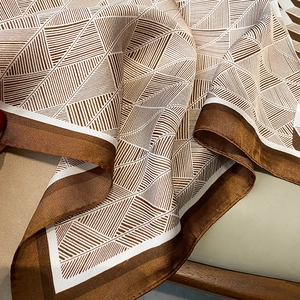 Detail of silk-like square scarf featuring brown geometric triangle patterns and smooth texture