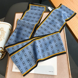 Dettaglio di un foulard in seta azzurro con stampa a farfalla e borsa a mano bianca