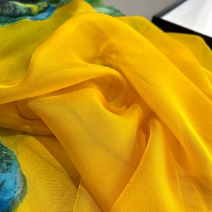 Close-up of lightweight yellow silk scarf with blue-green art print and soft texture