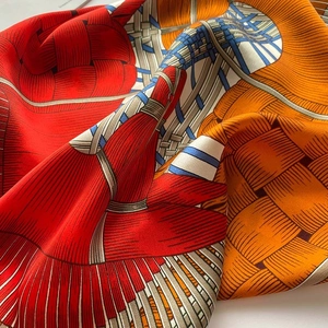 Close-up of silk square scarf featuring vibrant orange weave patterns and satin texture