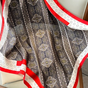 Detalle de un pañuelo de seda con estampado paisley y borde rojo en una silla