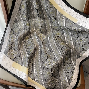 Primer plano de un pañuelo de seda estilo francés con motivos paisley y geométricos en silla