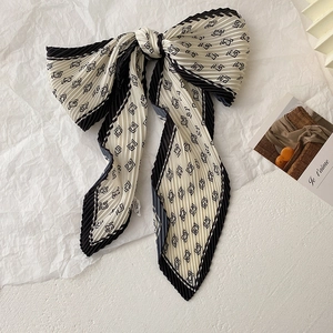 Détail du foulard plissé avec motifs géométriques noirs et blancs et nœud élégant