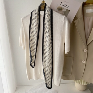Détail d'un foulard en soie plissé crème avec motif géométrique noir sur tricot