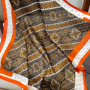 Detalle de pañuelo de seda con estampado barroco vintage y bordes en color naranja