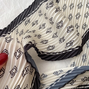 Détail macro du foulard plissé blanc avec logo G noir et bordure rayée élégante