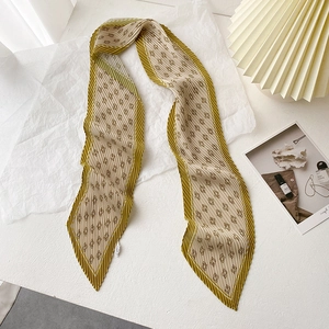 Détail d'un foulard plissé vert olive et beige avec imprimé monogramme géométrique
