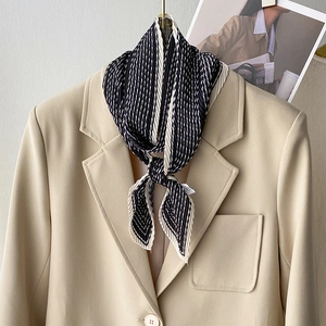 Sciarpa plissettata a righe bianche e nere su un blazer beige, accessorio di moda chic