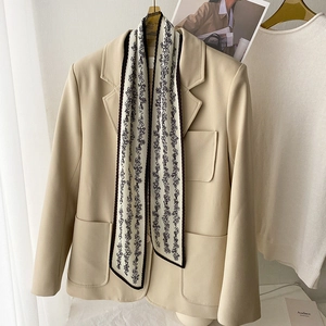 Detail of elegant slim silk scarf with black floral patterns and wavy edges on a blazer