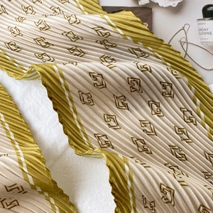 Détail d'un foulard en soie plissé avec motifs géométriques vert et beige au fini satiné