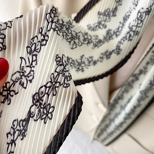 Close-up of pleated floral silk scarf with black vine patterns and wavy edges