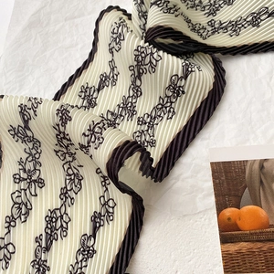 Detailed view of micro-pleated floral silk scarf with black contrast edges and beige base